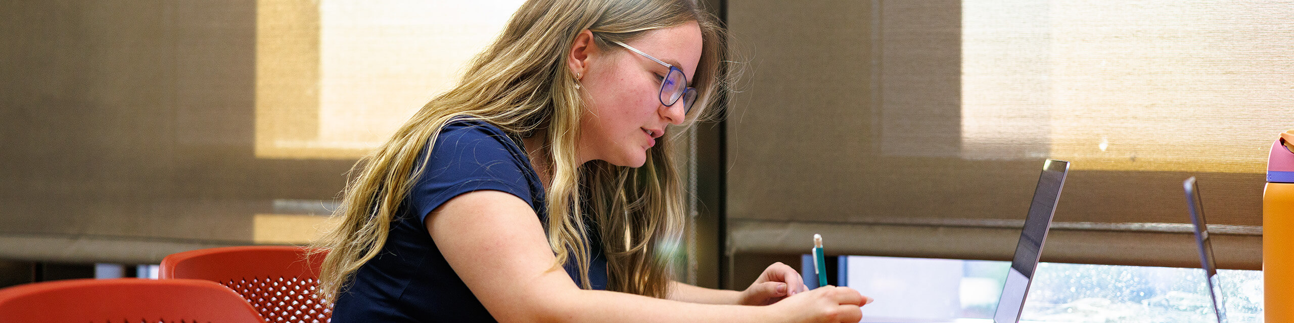 A student writes on a notebook and looks at laptop while studying in the library.
